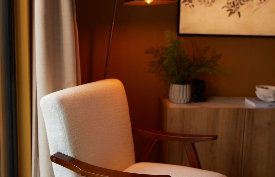 A quiet consulting room: a pale armchair, warm lamplight, wooden floor